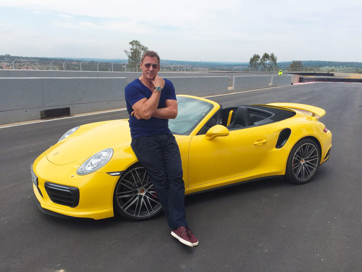 Ralf Möller steht vor seinem gelben Porsche auf einer Rennstrecke.