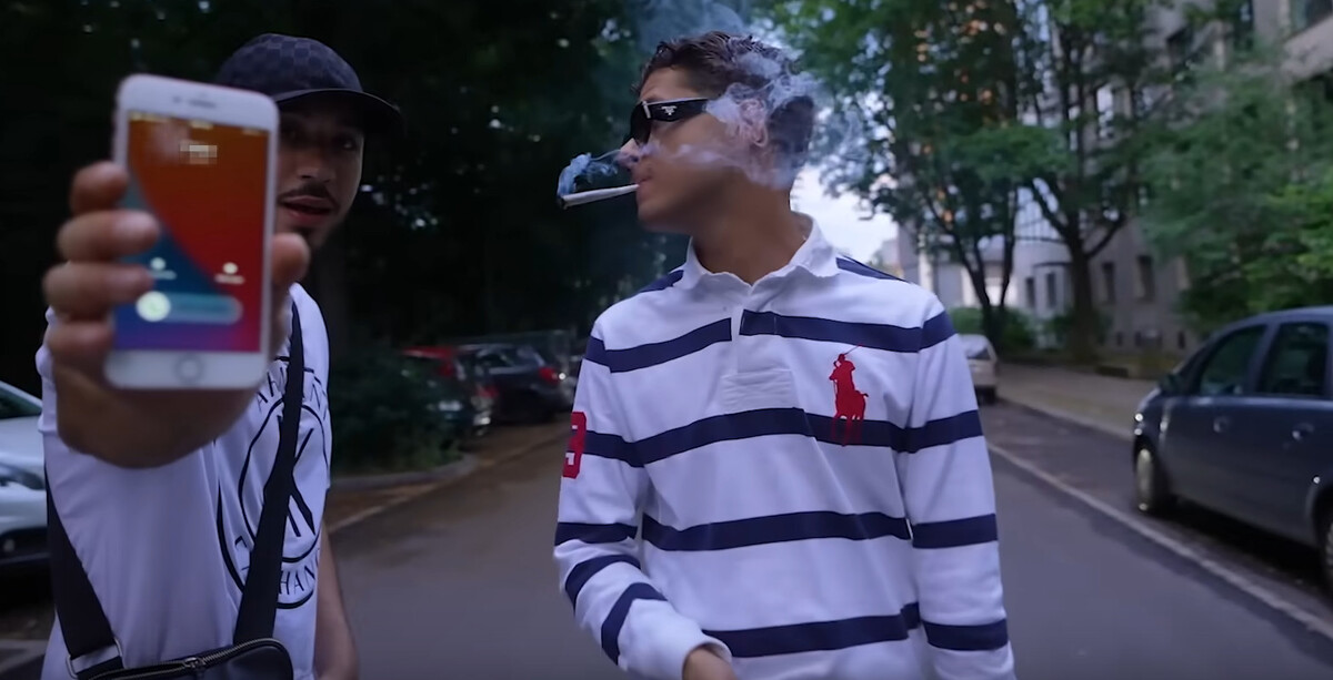 Rapper Pashanim läuft eine Straße entlang und raucht eine Zigarette.